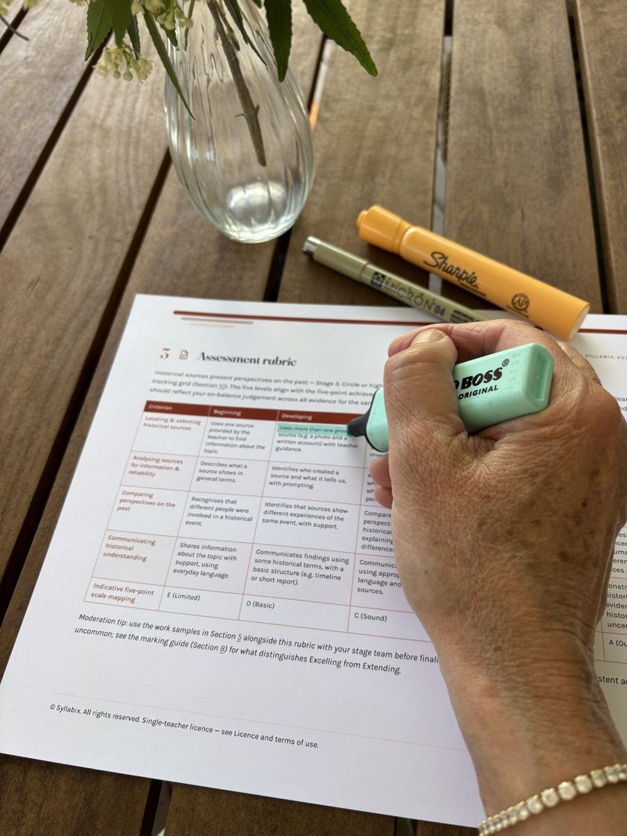 A hand highlighting a descriptor on the printed rubric